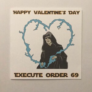 May include: Square white card with a cartoon image of a character in a black hooded robe inside a blue lightning bolt heart. The text "HAPPY VALENTINE'S DAY" is above the heart, and "EXECUTE ORDER 69" is below.