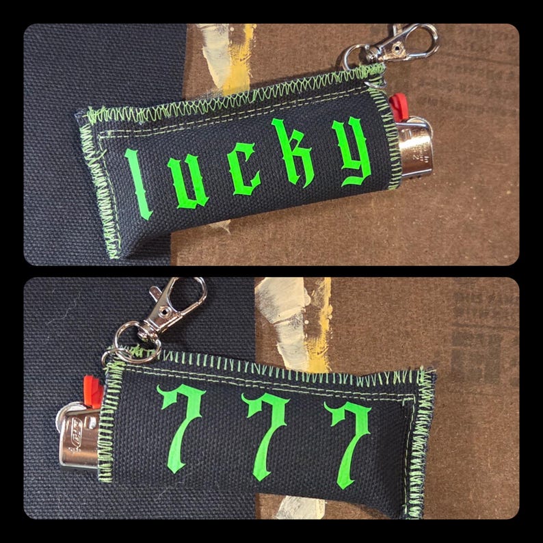 May include: A black fabric lighter sleeve featuring bright green stitched edges and a metal lobster clasp. One side displays the word lucky in a gothic font, while the reverse side features the number 777 in the same green gothic lettering.