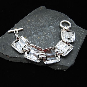May include: A silver bracelet with a hammered finish and square links. The bracelet has a toggle clasp.