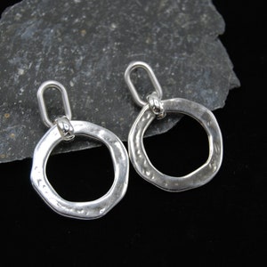 May include: A pair of silver hoop earrings with a hammered texture. The hoops are open and have a small loop at the top for hanging.