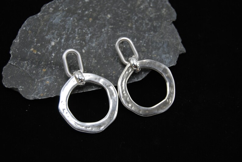 May include: A pair of silver hoop earrings with a hammered texture. The hoops are open and have a small loop at the top for hanging.