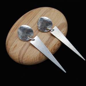 Puede incluir: Un par de pendientes de plata con un disco martillado y un colgante triangular.