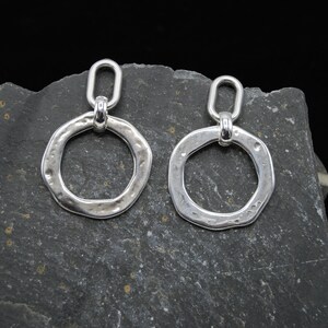 May include: A pair of silver earrings with a hammered, circular design. The earrings have a simple, oval-shaped loop at the top for hanging.