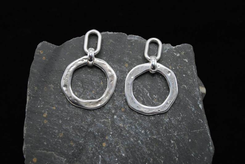 May include: A pair of silver earrings with a hammered, circular design. The earrings have a simple, oval-shaped loop at the top for hanging.