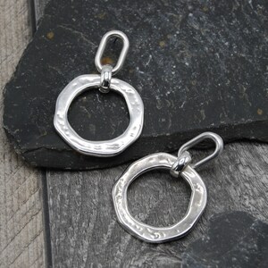 May include: A pair of silver earrings with a hammered texture and a circular design. The earrings have a simple, modern style.