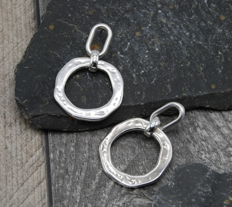 May include: A pair of silver earrings with a hammered texture and a circular design. The earrings have a simple, modern style.