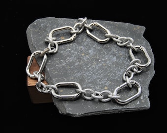 May include: A silver chain bracelet with multiple oval-shaped links. The bracelet is made of a braided metal chain and has a polished finish.