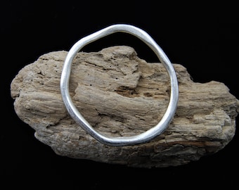 May include: A silver bangle bracelet with an irregular, organic shape. The bracelet is resting on a piece of driftwood.