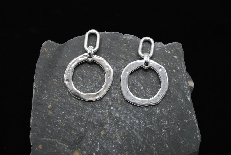 May include: A pair of silver earrings with a hammered, textured, circular design. Each earring has a small loop at the top for attaching to a hook.