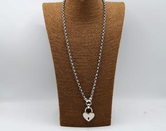 May include: Silver necklace with a heart-shaped padlock pendant. The necklace has a long chain with circular links. The pendant features a keyhole detail. The necklace is displayed on a brown bust form against a white backdrop.