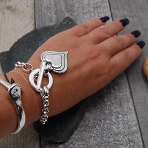 May include: A silver bracelet with a heart-shaped charm and a toggle clasp.