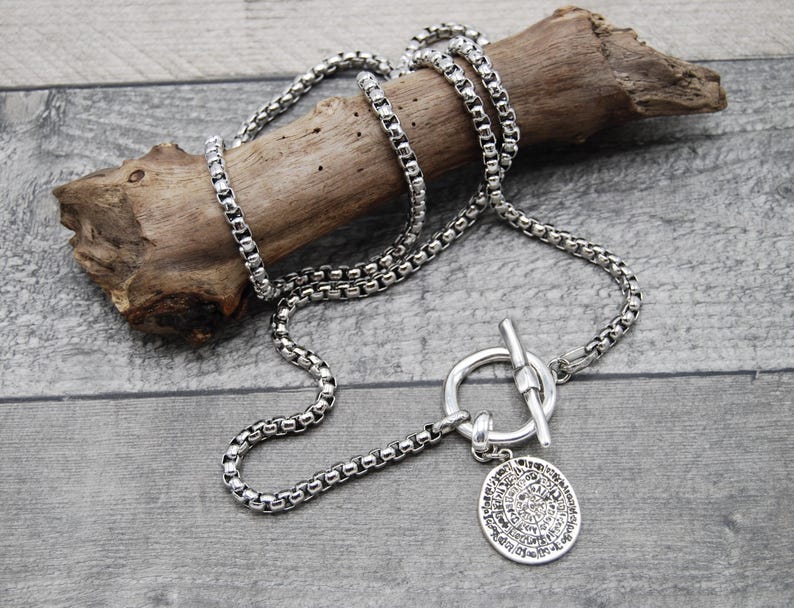 May include: A silver chain necklace with a toggle clasp and a round pendant with an intricate design.
