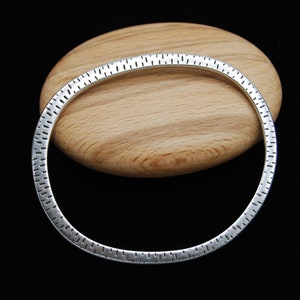 May include: A silver bangle bracelet with a textured design. The bracelet is round and has a smooth, polished finish.