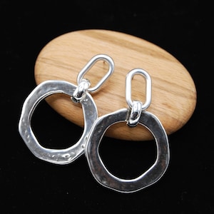 May include: A pair of silver dangle earrings with a hammered, textured, oval-shaped design. Each earring features a smaller, linked oval loop.