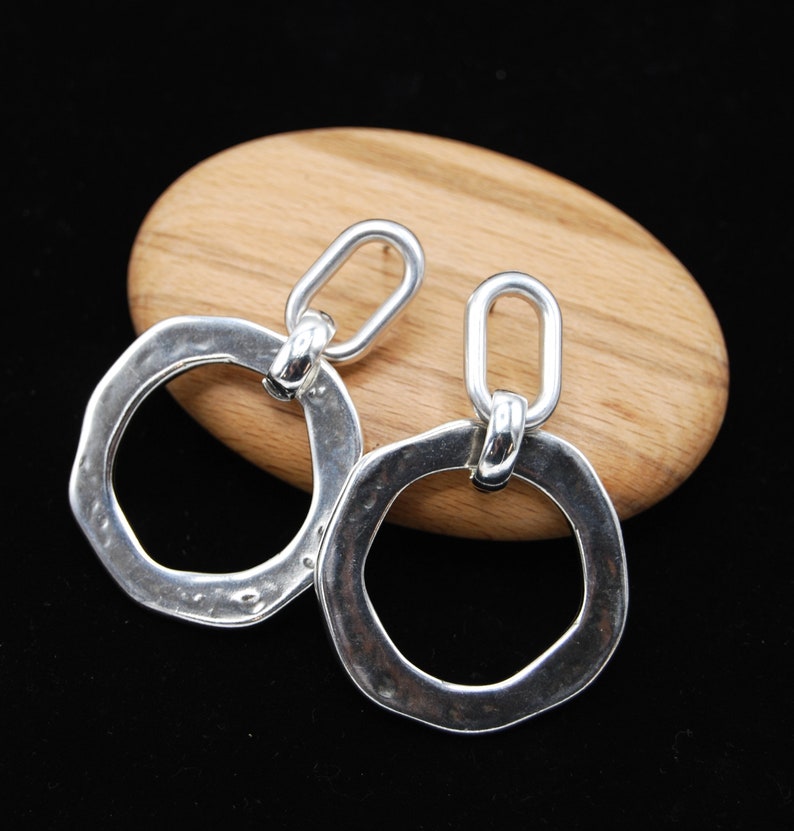 May include: A pair of silver dangle earrings with a hammered, textured, oval-shaped design. Each earring features a smaller, linked oval loop.