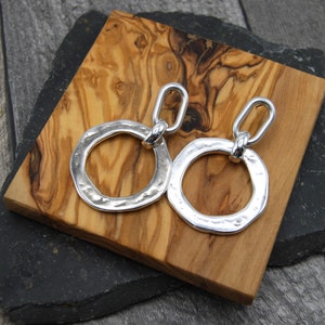 May include: Silver dangle earrings with a hammered, circular design. The earrings have a linked chain detail.