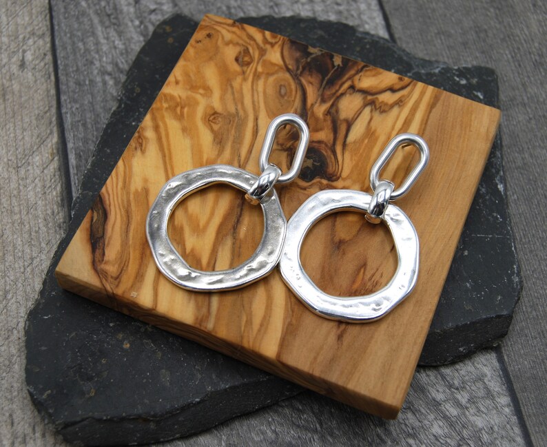 May include: Silver dangle earrings with a hammered, circular design. The earrings have a linked chain detail.