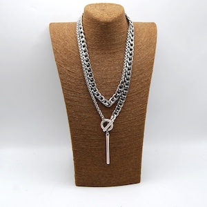 May include: A silver layered chain necklace with a long, thin pendant and a toggle clasp.