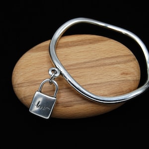 Könnte beinhalten: Ein silbernes Armreif-Armband mit einem silbernen Vorhängeschloss-Anhänger, auf dem "love" steht.