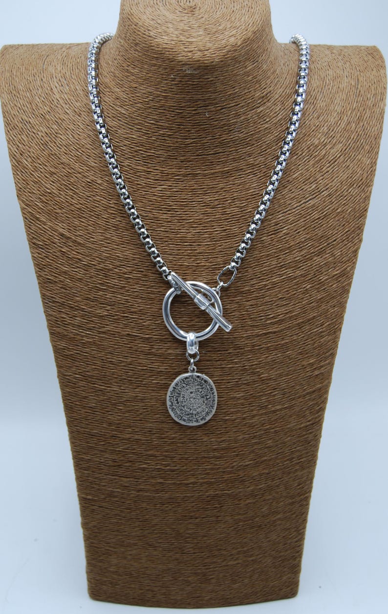 May include: A silver chain necklace with a toggle clasp and a round pendant featuring an intricate design.