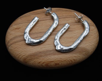 May include: A pair of silver hoop earrings with a textured, hammered finish. The hoops are oval shaped and have a slightly open design.