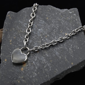 Puede incluir: Un collar de plata con un candado en forma de corazón y una cadena de plata.