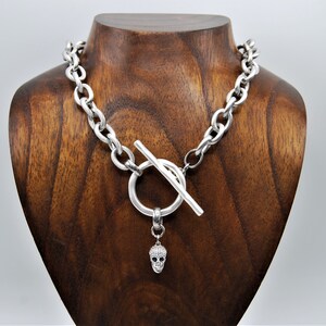 Peut inclure: Un collier en chaîne argentée avec un fermoir à bascule et un pendentif en forme de crâne. Le pendentif est orné de petits cristaux transparents.