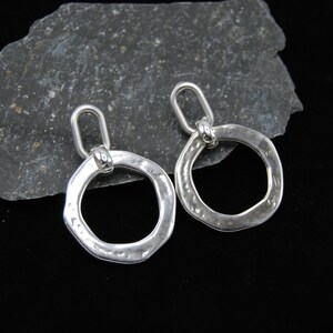 May include: A pair of silver earrings with a hammered, circular design. Each earring has a small loop at the top for attaching to an ear wire.