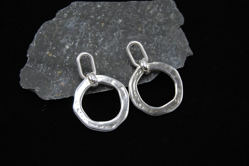 May include: A pair of silver earrings with a hammered, circular design. Each earring has a small loop at the top for attaching to an ear wire.