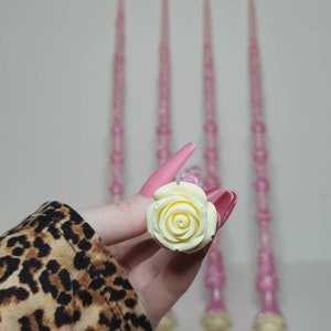 May include: Four pink wands with white rose-shaped tops. The wands are made of a sparkly material and have a delicate, feminine look.