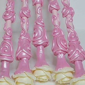 May include: Six pink and white decorative wands with a rose design. The wands are made of a smooth, shiny material and have a delicate, feminine look.