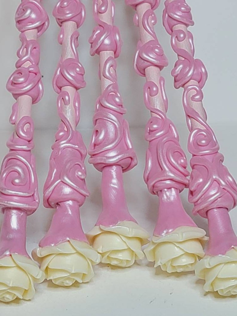 May include: Six pink and white decorative wands with a rose design. The wands are made of a smooth, shiny material and have a delicate, feminine look.