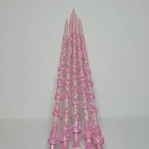 May include: A set of seven pink wands with white rose accents. The wands are decorated with a swirling, floral pattern.