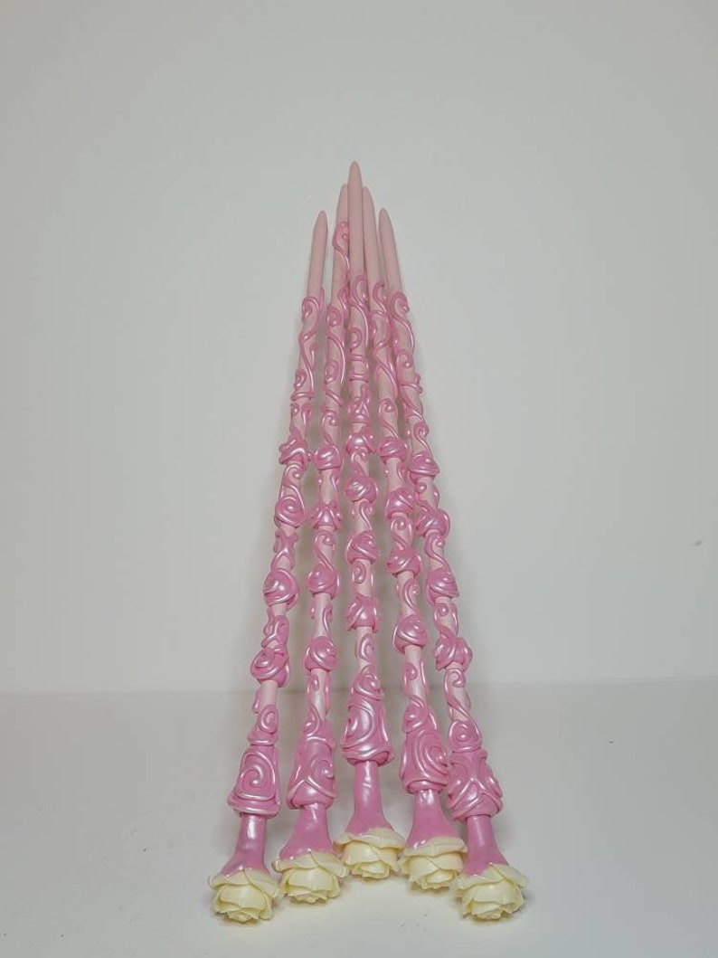 May include: A set of seven pink wands with white rose accents. The wands are decorated with a swirling, floral pattern.