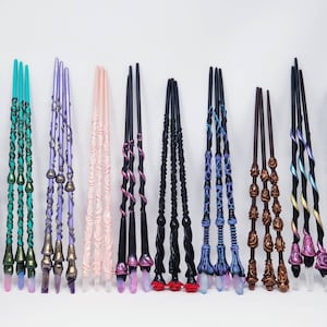 May include: A selection of handcrafted wands in diverse colours, such as blue, green, purple, and pink. Each wand has unique spiral and decorative designs, with crystal-like tips. The wands are displayed against a white backdrop.