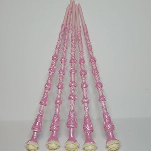 May include: Six pink wands with white rose accents. The wands are decorated with a swirling rose pattern.