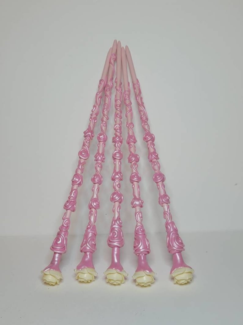 May include: Six pink wands with white rose accents. The wands are decorated with a swirling rose pattern.