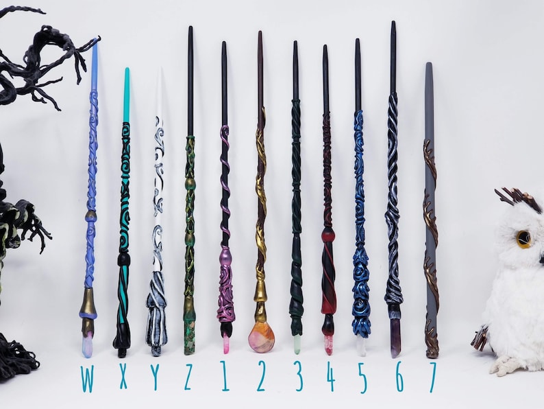 May include: A selection of handcrafted wands in diverse colours and designs. Each wand has unique details, including carved patterns, crystal accents, and metallic finishes. The wands are labelled with letters and numbers.