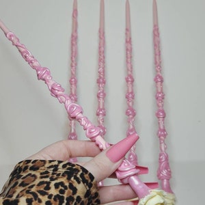 May include: Five pink wands with a rose design. The wands are made of a smooth, shiny material and have a white rose at the end.