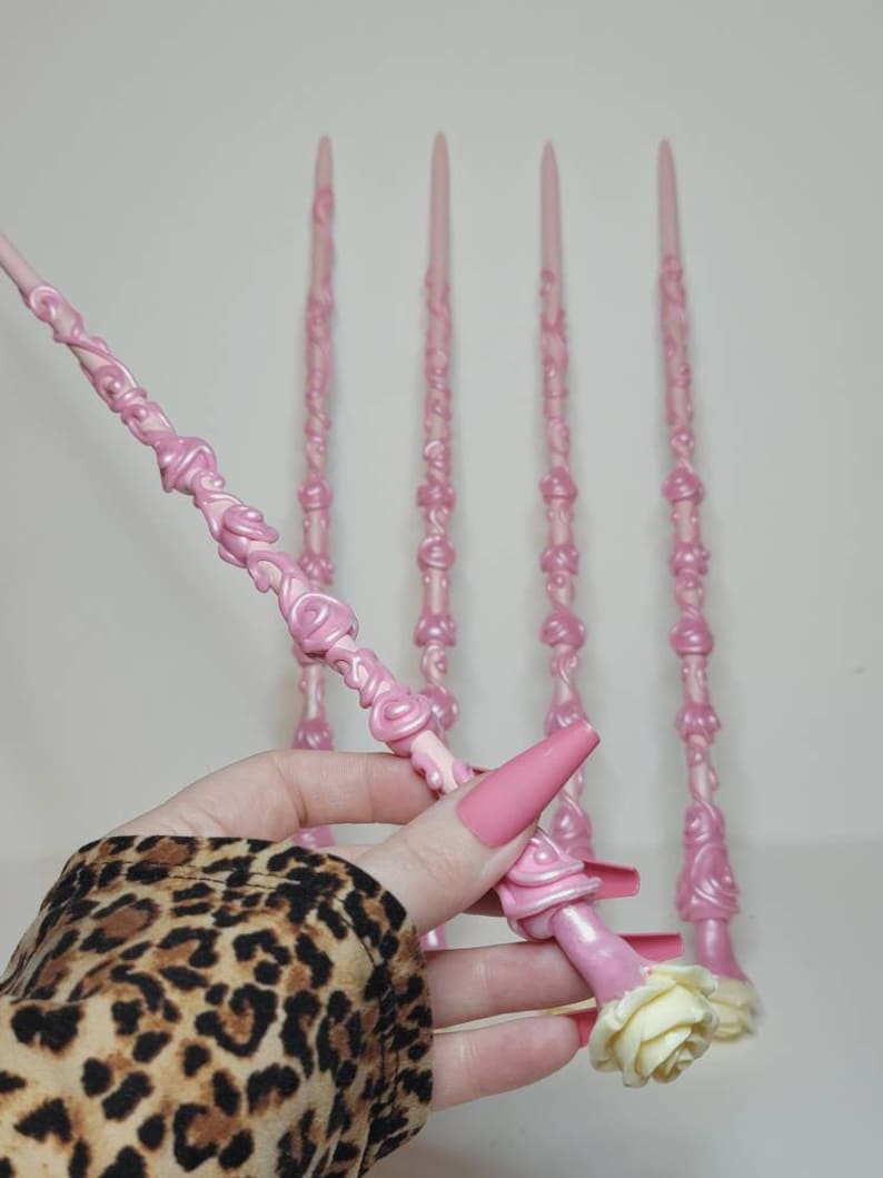 May include: Five pink wands with a rose design. The wands are made of a smooth, shiny material and have a white rose at the end.