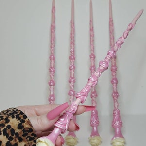 May include: Five pink wands with white rose details. The wands are intricately designed with swirls and are made of a smooth, glossy material.
