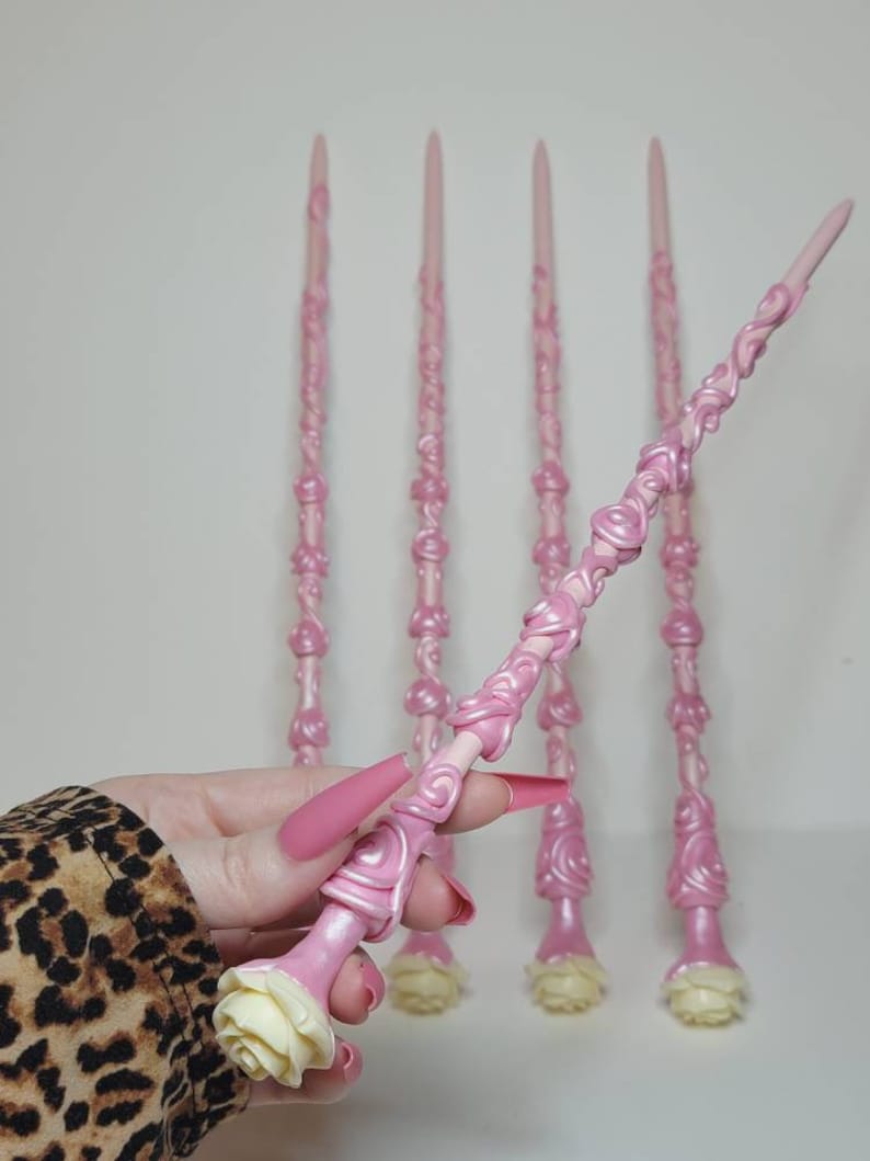 May include: Five pink wands with white rose details. The wands are intricately designed with swirls and are made of a smooth, glossy material.