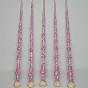 May include: Five pink wands with white rose accents. The wands are decorated with a swirling, rose-like pattern.