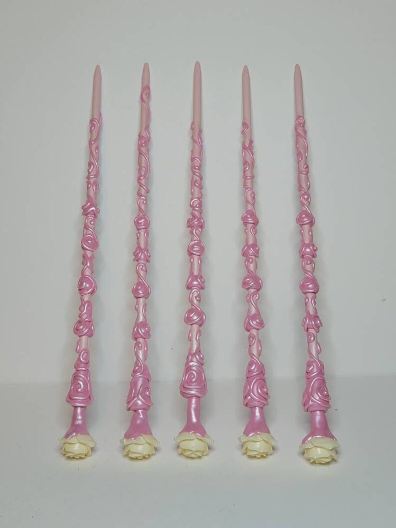 May include: Five pink wands with white rose accents. The wands are decorated with a swirling, rose-like pattern.