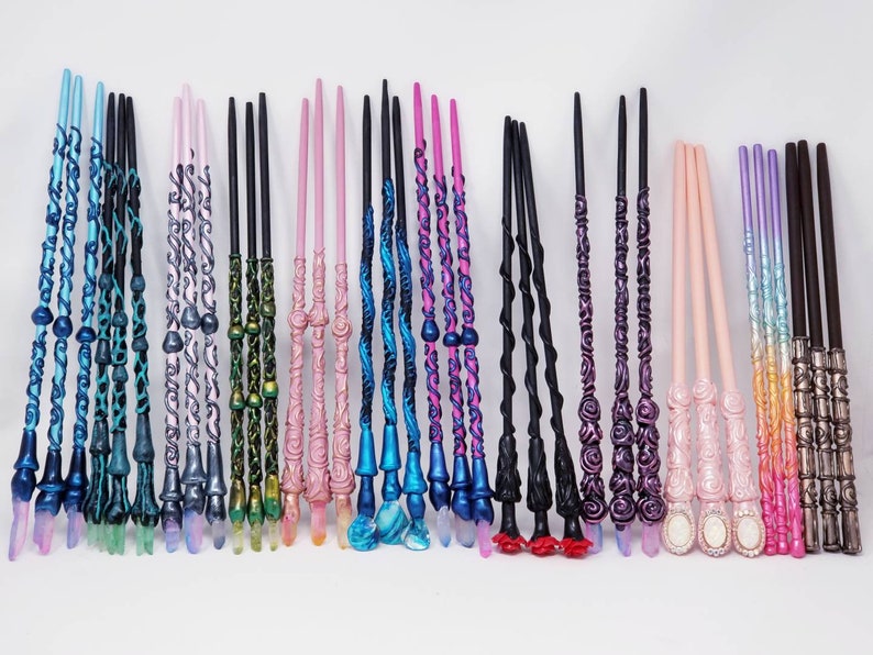 May include: A selection of decorative wands in shades of blue, pink, black, and purple. Each wand has detailed patterns, crystal-like tips, and ornate handles. The wands are displayed in a row, highlighting their individual designs and styles.