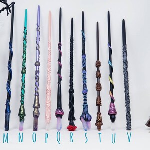 May include: Eleven handcrafted wands in a variety of colours and designs. Each wand has unique details, including swirling patterns, crystal accents, and carved textures. The wands are labelled with the letters M through V.