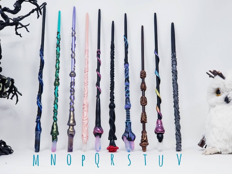 May include: Eleven handcrafted wands in a variety of colours and designs. Each wand has unique details, including swirling patterns, crystal accents, and carved textures. The wands are labelled with the letters M through V.