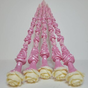 May include: A set of seven pink and white wands with a rose design. The wands are made of polymer clay and have a swirl pattern. The roses are white and have a realistic look.