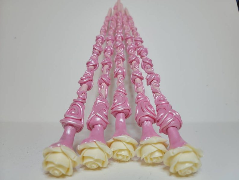 May include: A set of seven pink and white wands with a rose design. The wands are made of polymer clay and have a swirl pattern. The roses are white and have a realistic look.
