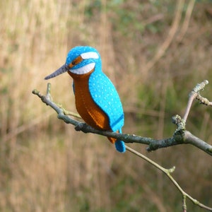May include: A blue and orange felt bird perched on a branch. The bird has a long, thin beak and white markings on its face.
